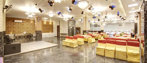 A spacious hall with rows of yellow and red-covered chairs, chandeliers, and ceiling fans.