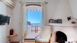 Una habitación con televisión, estantería, chimenea y vista al mar.
