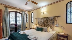 Habitación de hotel con una cama grande, cabecera con tapiz, mesita de noche con lámpara y ventana con cortinas.