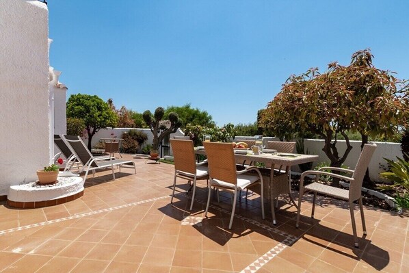 An outdoor patio with a table and chairs, surrounded by potted plants and a tree.