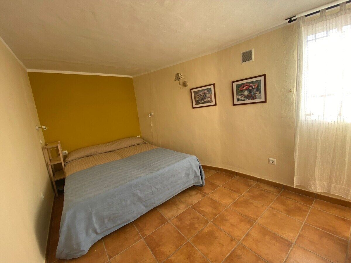 A small bedroom with a bed, a chair, and two framed pictures on the wall.