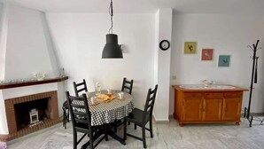 Un'area pranzo con tovaglia a scacchi, sedie nere, un lampadario, un mobiletto in legno e un orologio appeso al muro.