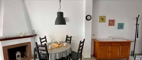 A dining area with a checkered tablecloth, black chairs, a hanging light fixture, a wooden cabinet, and a clock on the wall.