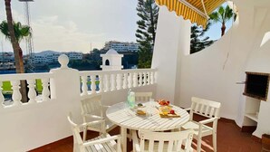 Un patio con tavolo e sedie bianche, un tendone a righe e vista su edifici e alberi.