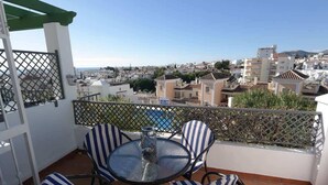 Un balcon avec une table ronde et des chaises à rayures, donnant sur un quartier résidentiel avec des immeubles et un ciel dégagé.