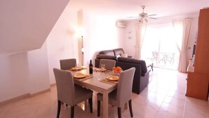 A dining area with a table set for four, a sofa, and a ceiling fan in a bright room with a tiled floor. - SHR010 Spacious apartment with pool near the beach (Nerja)