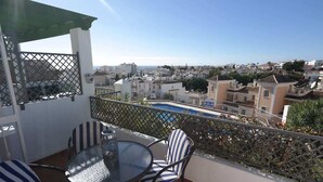 A balcony with a glass table and striped chairs, overlooking a residential area and a pool. - SHR010 Spacious apartment with pool near the beach (Nerja)