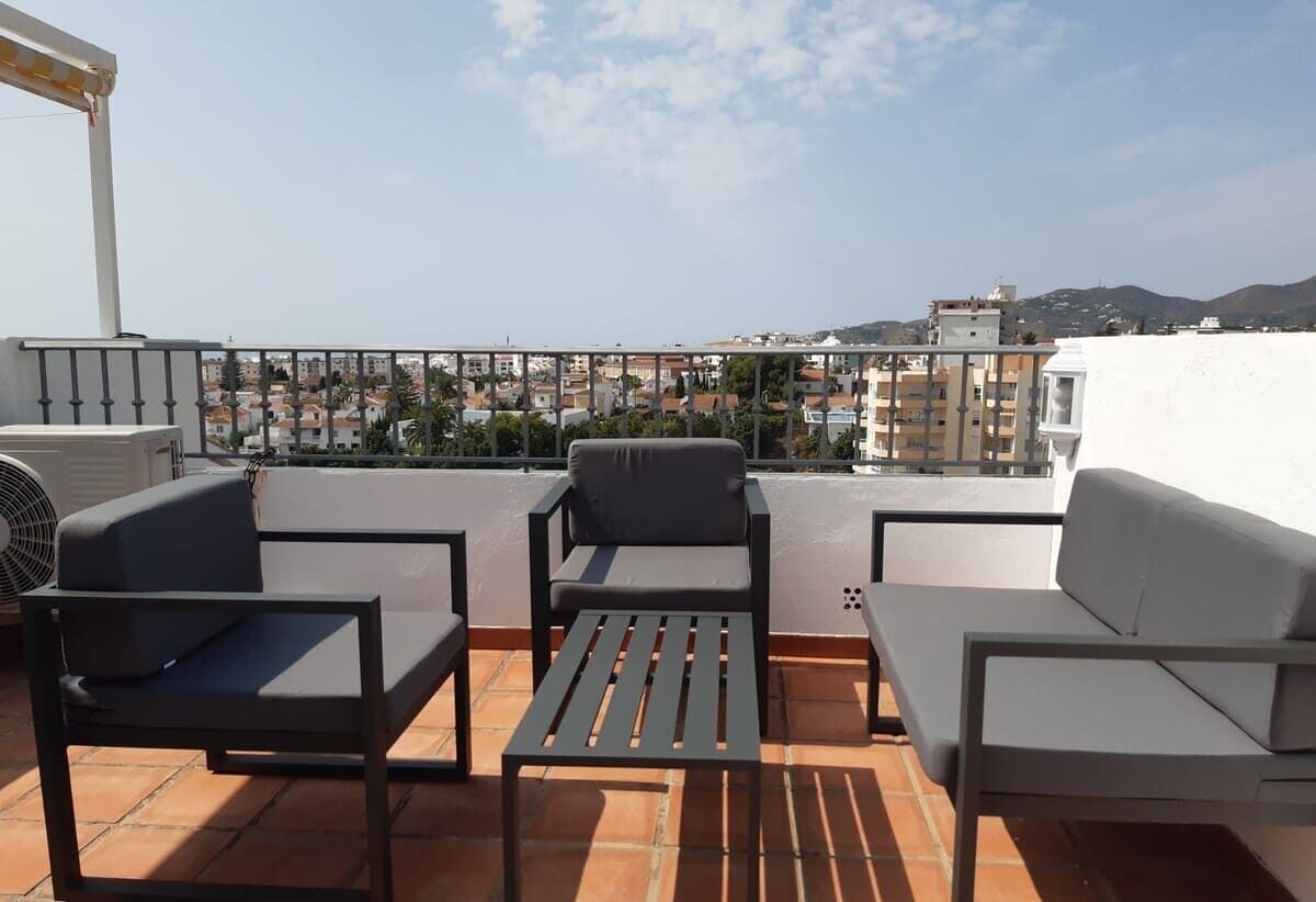 A rooftop terrace with outdoor furniture, a view of the cityscape, and a white building in the background.