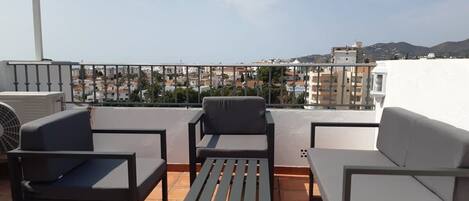 A rooftop terrace with outdoor furniture, a view of the cityscape, and a white building in the background.