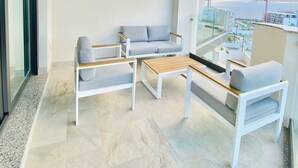 Un balcón moderno con techo de madera, mobiliario blanco y vista a la ciudad.
