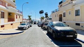 A street with parked cars and buildings on either side, under a clear blue sky.