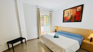 A hotel room with a bed, a bench, a nightstand, a lamp, and a painting on the wall.