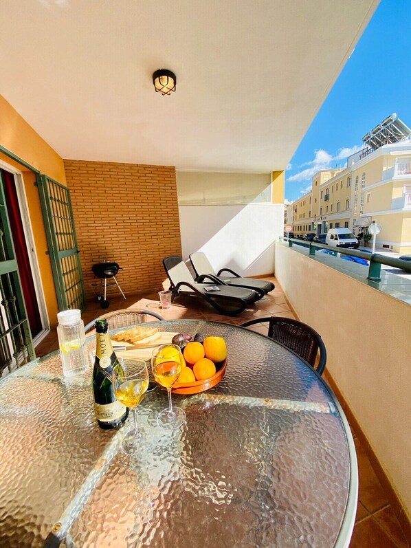 A glass table with a bottle of Moët & Chandon champagne, a glass of wine, and a bowl of oranges on a balcony overlooking a cityscape.