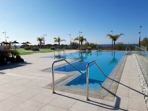 Ein Schwimmbad mit freiem Blick auf den Ozean, umgeben von Palmen und einer gefliesten Terrasse.