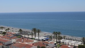 A coastal view with a beach, palm trees, and buildings with red-tiled roofs. - SHR019 Gran Atico al lado de la playa (Torrox Costa)