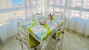 A corner room with a table and chairs, large windows with curtains, and a view of buildings and a body of water. - SHR019 Gran Atico al lado de la playa (Torrox Costa)