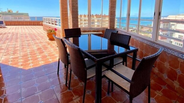 A covered patio with a table and chairs, large windows, and a view of the sea. - SHR019 Gran Atico al lado de la playa (Torrox Costa)