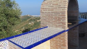 A brick chimney with a tiled roof, overlooking a hilly landscape.