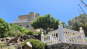 A stone building with a balcony, surrounded by greenery and rocks. - SHR018 Villa El Castillo (Torrox)