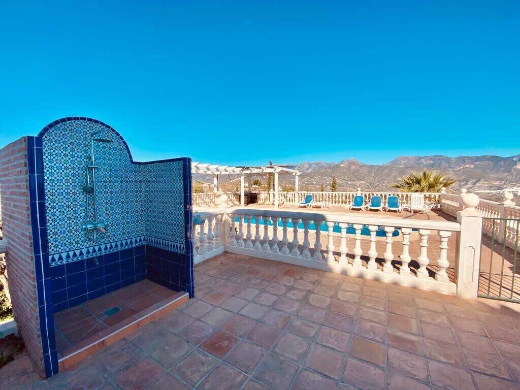 Une terrasse sur le toit dotée d’une cabine de douche aux carreaux bleus, d’une piscine avec des chaises longues et d’une vue sur les montagnes lointaines.