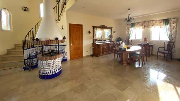 A spacious living area with a central staircase, a dining table, and a kitchen area.