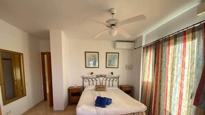 A bedroom with a bed, a ceiling fan, a window with curtains, and a door.