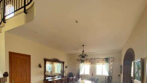 A spacious living area with a dining table, chairs, a staircase, and a kitchen area.