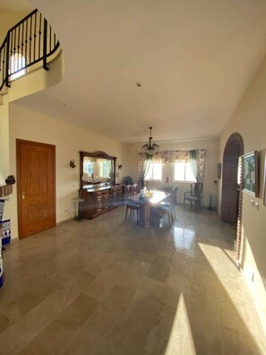 A spacious living area with a dining table, chairs, a staircase, and a kitchen area. - SHR018 Villa El Castillo (Torrox)