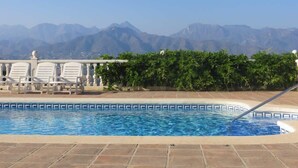 A swimming pool with a view of mountains, surrounded by a tiled deck and white lounge chairs.
