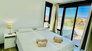 Ein Hotelzimmer mit zwei Betten, einem Nachttisch, einer Lampe und einem großen Fenster mit Blick.