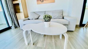 Ein modernes Wohnzimmer mit einem grauen Sofa, einem weißen Couchtisch und einer Topfpflanze.