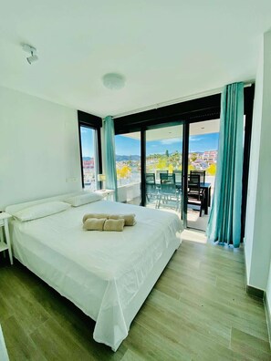 Une chambre d’hôtel avec un grand lit, un balcon doté d’une table et de chaises, et une vue sur la ville.