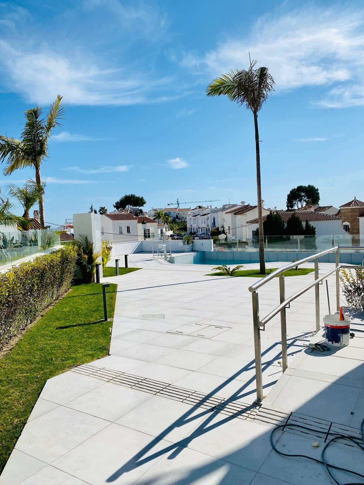 Ein moderner Außenbereich mit einer Metalltreppe, einem Betonweg und freiem Blick auf Wohnhäuser im Hintergrund.