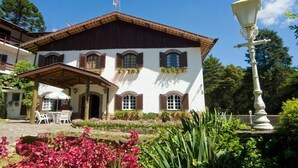 A traditional building with a tiled roof, arched windows, and a covered patio area with outdoor seating. - Hotel Terrazza (Campos do Jordão)