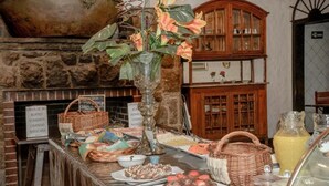A buffet setup with various food items, a large vase with flowers, and a rustic stone wall in the background. - Hotel Terrazza (Campos do Jordão)