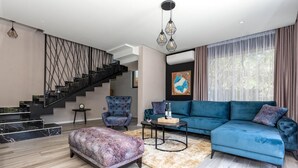 A modern living room with a blue sofa, patterned ottoman, and a staircase with a geometric railing. - Gorgeous home in Kremena (Kremena)