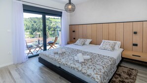A bedroom with a large bed, a wooden headboard, a balcony with a table and chairs, and a view of greenery outside. - Gorgeous home in Kremena (Kremena)