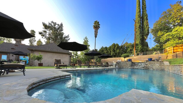 A swimming pool with stone tiles, surrounded by lounge chairs and umbrellas. - Luxury Suite "A" (Redlands)