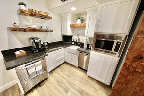 A modern kitchen with white cabinets, a stainless steel dishwasher, a built-in microwave, and wooden shelves.