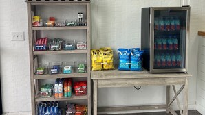 A room with a wooden shelf displaying various snacks and drinks, a refrigerator with Fiji water, and a sign indicating 'SEA ISLE CITY, NEW JERSEY'. - The Ludlam (Sea Isle City)