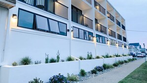 A multi-story hotel with balconies, a white exterior, and a landscaped garden area. - The Ludlam (Sea Isle City)