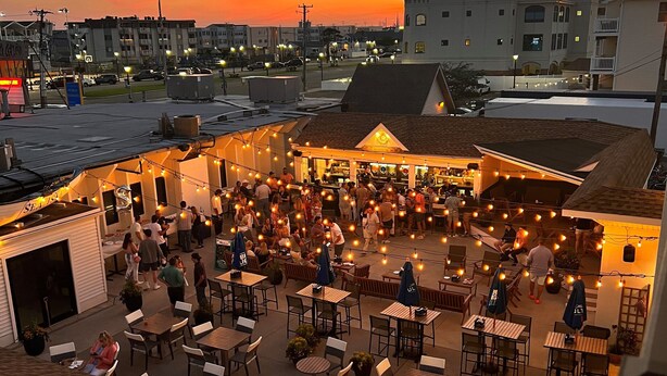An outdoor patio area with tables and chairs, surrounded by buildings. - The Ludlam (Sea Isle City)