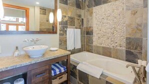 Ein Badezimmer mit einer Steinwand, einer Badewanne, einem Waschbecken und einem Spiegel.