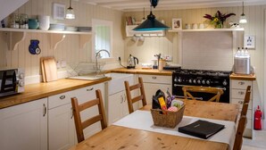 A kitchen with wooden cabinets, a stove, a microwave, and a dining table with chairs. - Kirk Wynd Cottage - Classic Charm (Angus)
