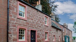 A stone building with pink window frames and a black door. - Kirk Wynd Cottage - Classic Charm (Angus)