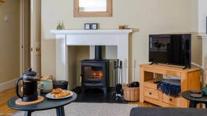 A cozy living room with a fireplace, a television, and a coffee table with pastries. - Kirk Wynd Cottage - Classic Charm (Angus)