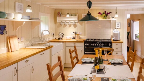 A kitchen with wooden cabinets, a dining table set for four, and a stove. - Kirk Wynd Cottage - Classic Charm (Angus)