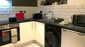 Uma cozinha compacta com armários brancos, lava-louças, micro-ondas e um tábua de corte vermelha.