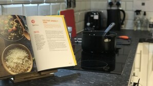 Uma bancada de cozinha com um livro de receitas aberto, uma panela e uma tigela de arroz.