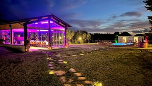 Un espace extérieur aménagé pour les repas, doté d’une structure vitrée, d’une piscine et de sentiers en pierre.